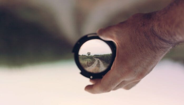 Man holding a lens that shows a dirt road right side up while the background is upside down