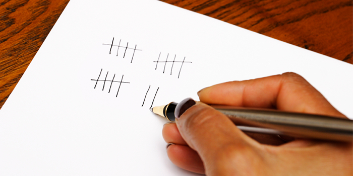 Woman's hand holding a pen writing tally marks on a piece of white paper
